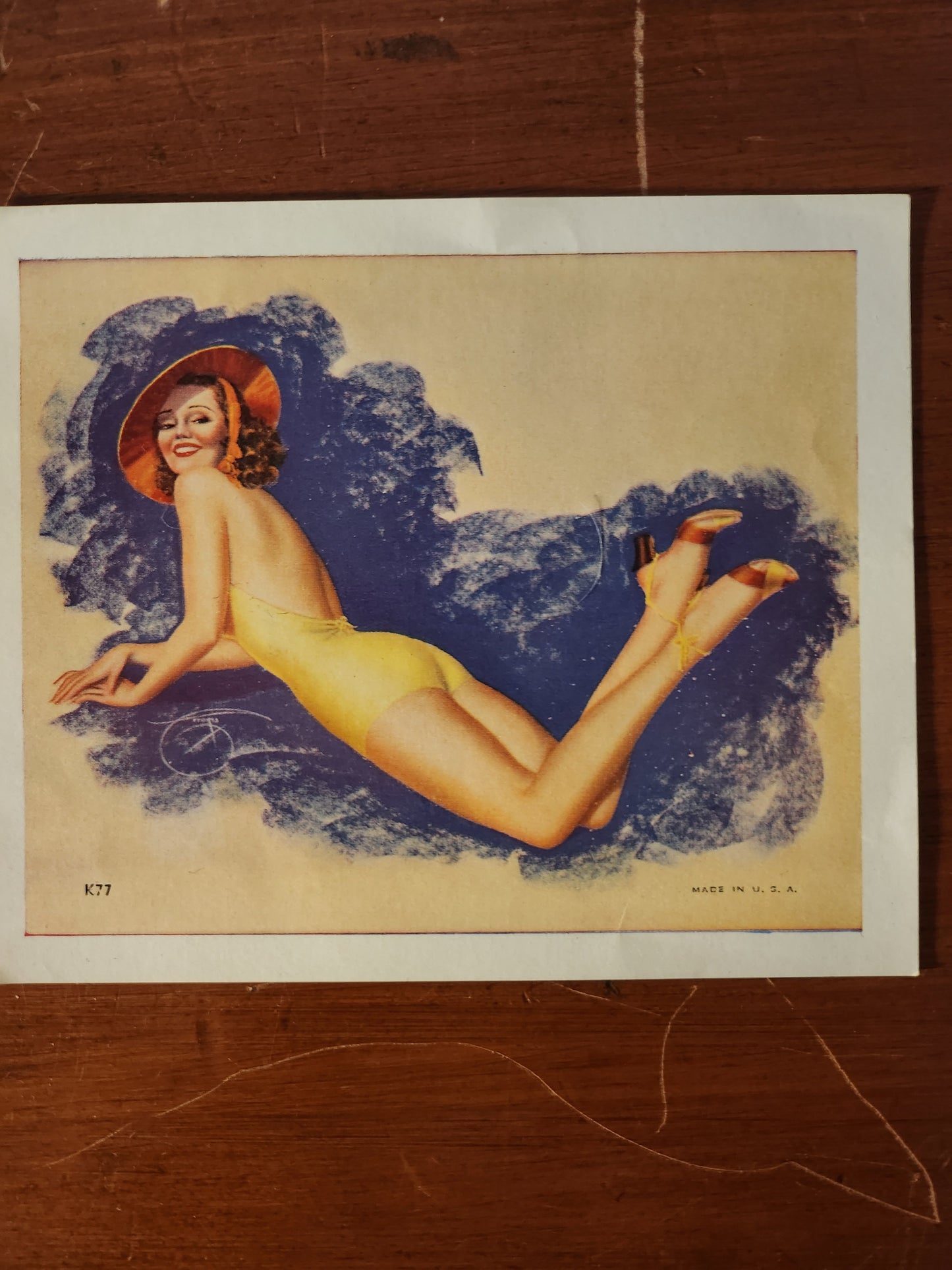 Postcard sized, vintage, pin-up model illustration of a woman in a yellow bathing suit with blue background 
