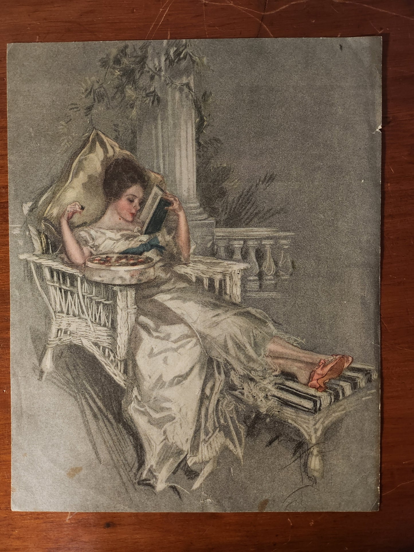 Vintage Harrison Fisher illustration of woman in a wicker chaise lounge
